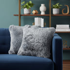 Gray fluffy pillows on a blue couch with a bookshelf in the background