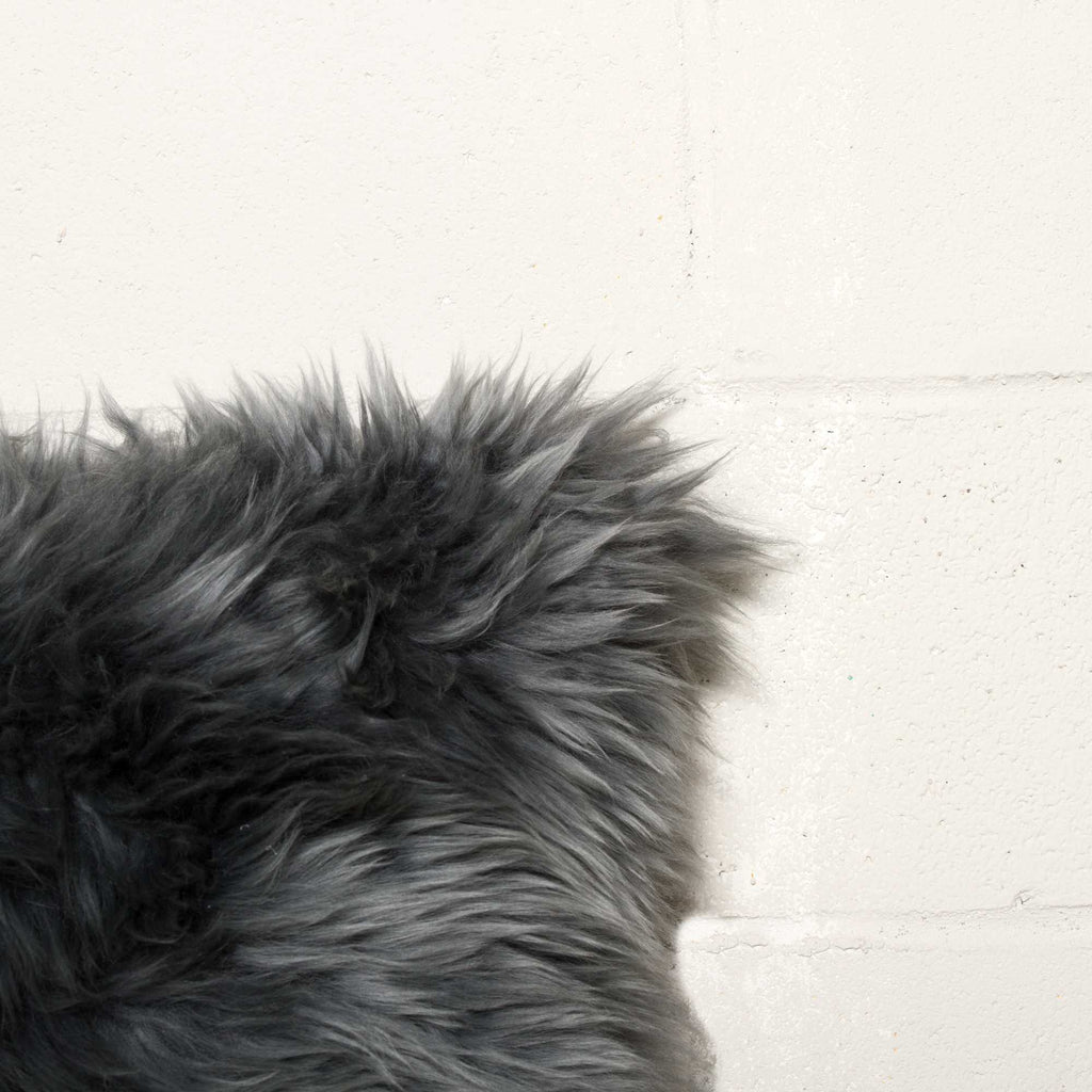Close-up of a dark gray fluffy rug on a light wooden floor.