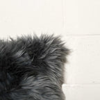 Close-up of a dark gray fluffy rug on a light wooden floor.