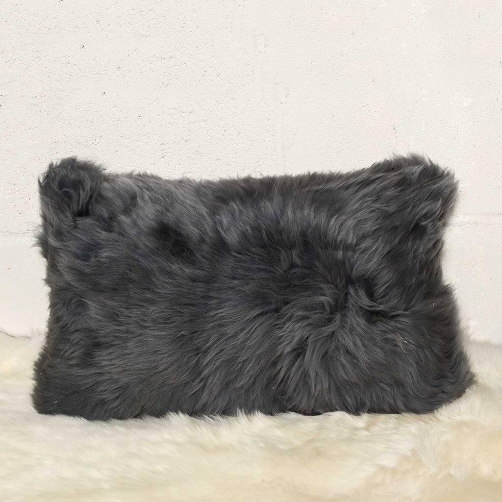 Gray fluffy pillow on a light beige surface with a neutral background