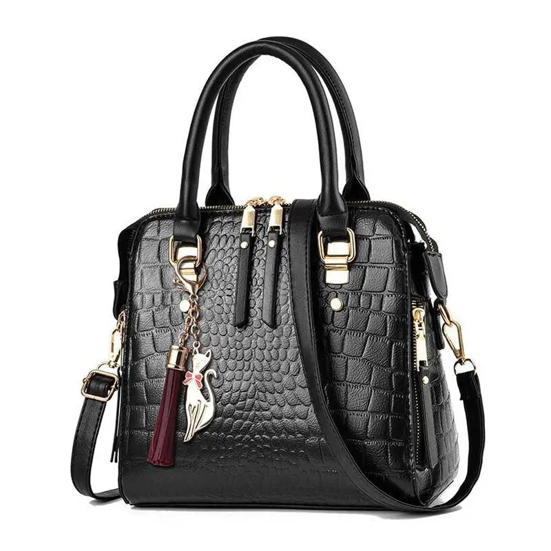 Black crocodile-embossed leather handbag with double top handles, gold-tone hardware, a detachable shoulder strap, and a hanging tassel charm on a white background.