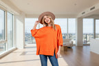 A female model wearing an orange side slit drop shoulder puff sleeve sweatshirt and a wide-brimmed hat.