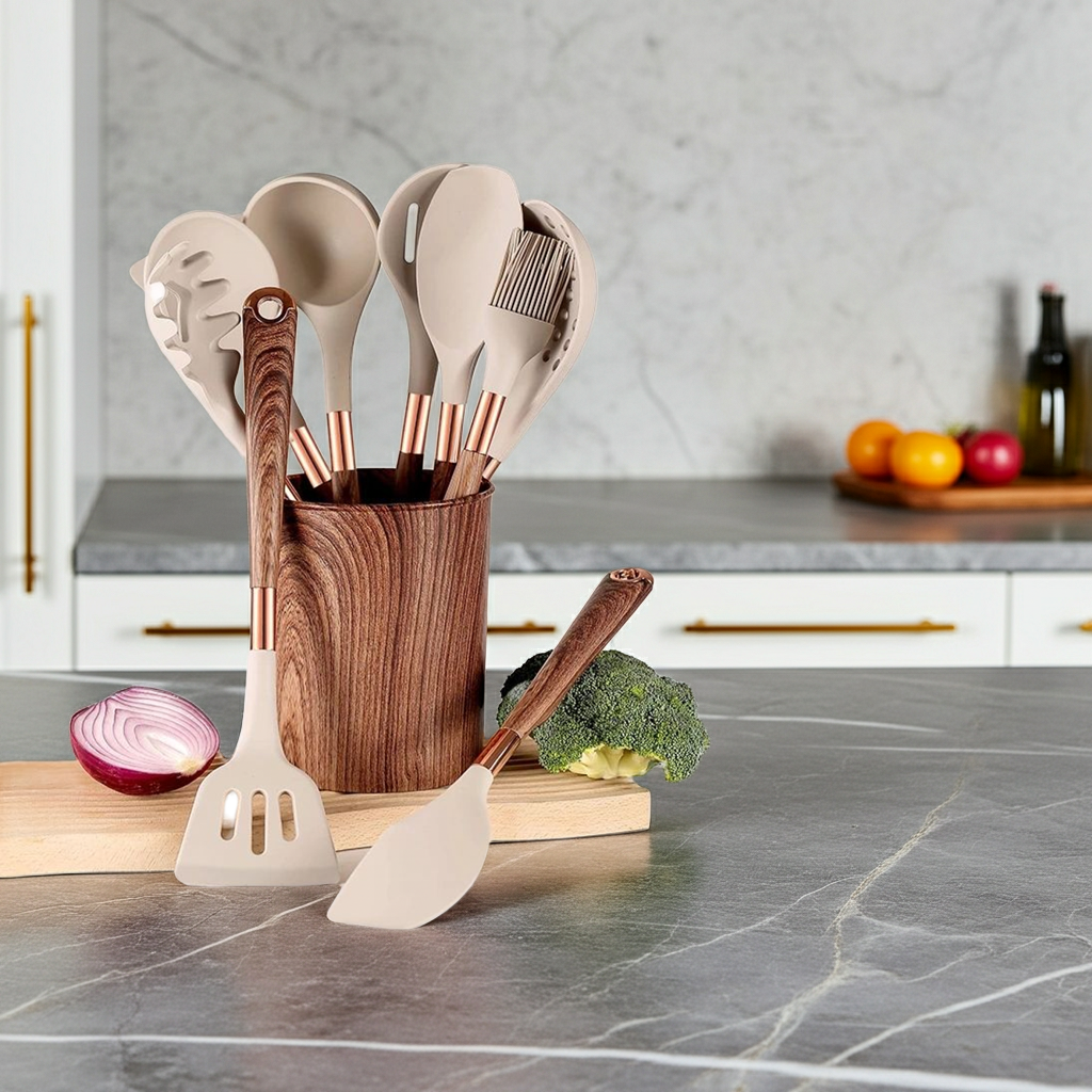 Set of kitchen utensils in a wooden holder on a kitchen counter with vegetables and fruit in the background.